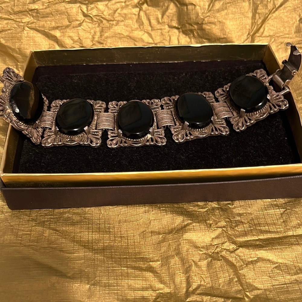 Black oval stones in a brass colored bracelet with clasp.